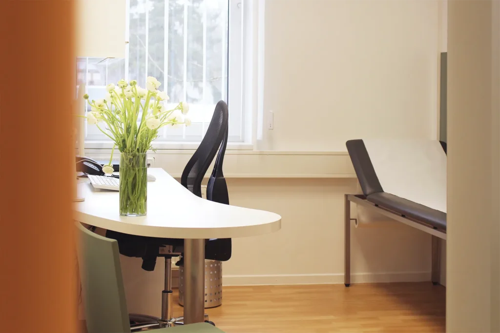 Helles und freundliches Sprechzimmer der Gastroenterologischen Gemeinschaftspraxis Bremen mit Schreibtisch und Liege.