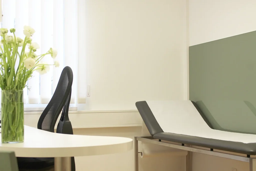 Helles und freundliches Sprechzimmer der Gastroenterologischen Gemeinschaftspraxis Bremen mit Schreibtisch und Liege.