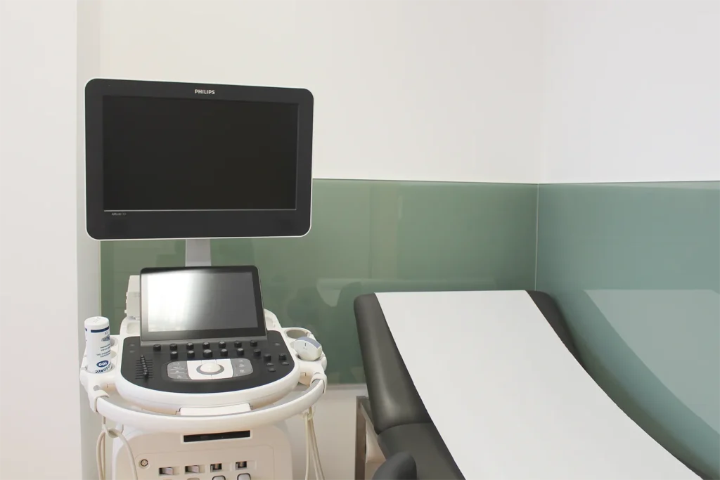 Ein modernes Ultraschallgerät der Praxis steht neben einer Liege im Behandlungszimmer.